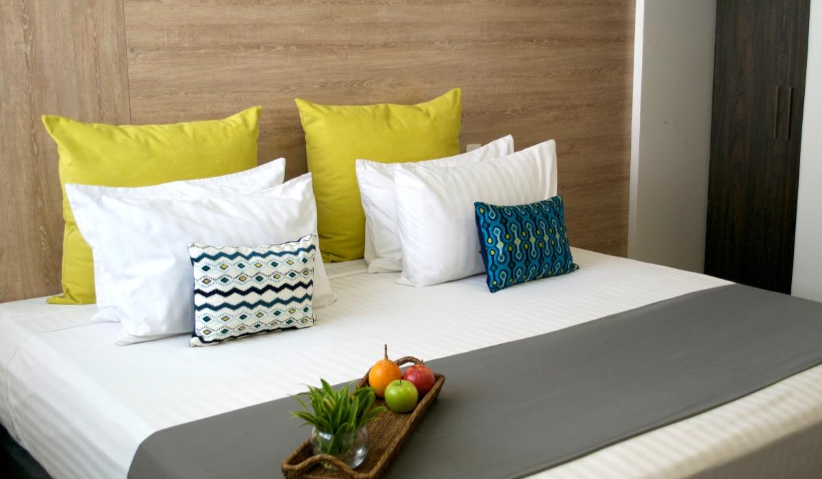 Habitación moderna con cama doble y decoración sofisticada en Hotel Casablanca Cúcuta. Habitación moderna con cama doble, cojines y bandeja con frutas en Hotel Casablanca Cúcuta