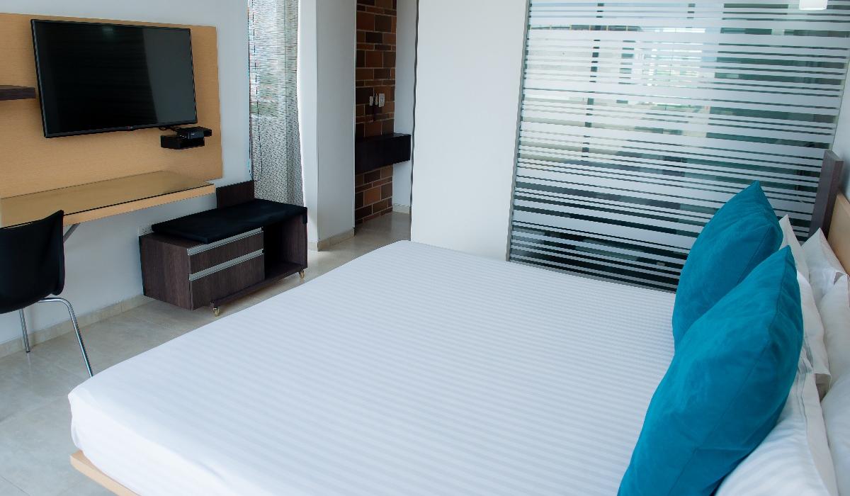 Habitación espaciosa con cama grande y TV en Hotel Casablanca Cúcuta. Habitación amplia con cama grande, cojines azules y TV en pared en Hotel Casablanca Cúcuta.