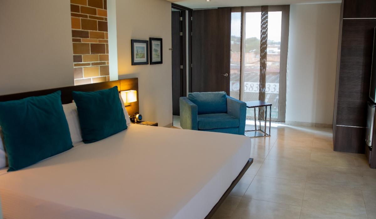 Habitación amplia y moderna con ventanales grandes en Hotel Casablanca Cúcuta. Habitación amplia con cama grande, sillón azul y ventanales en Hotel Casablanca Cúcuta.