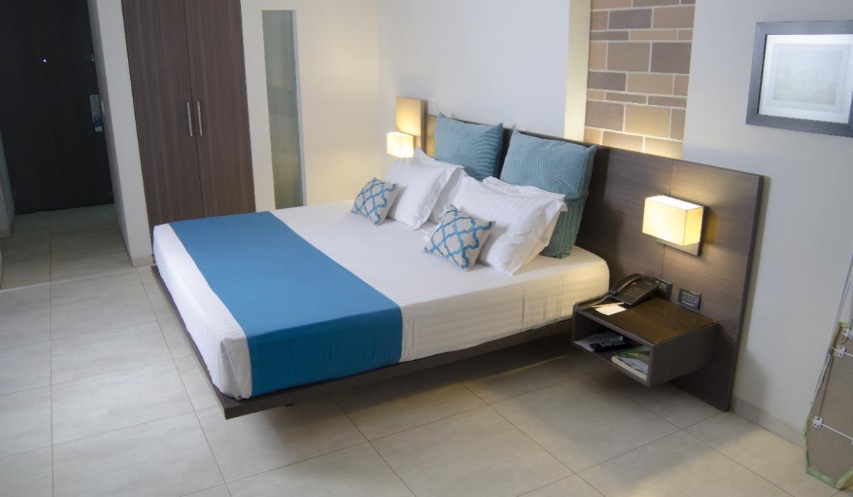 Habitación moderna con cama matrimonial y estilo elegante en Hotel Casablanca Cúcuta. Habitación con cama matrimonial, cojines azules y decoración moderna en Hotel Casablanca Cúcuta.