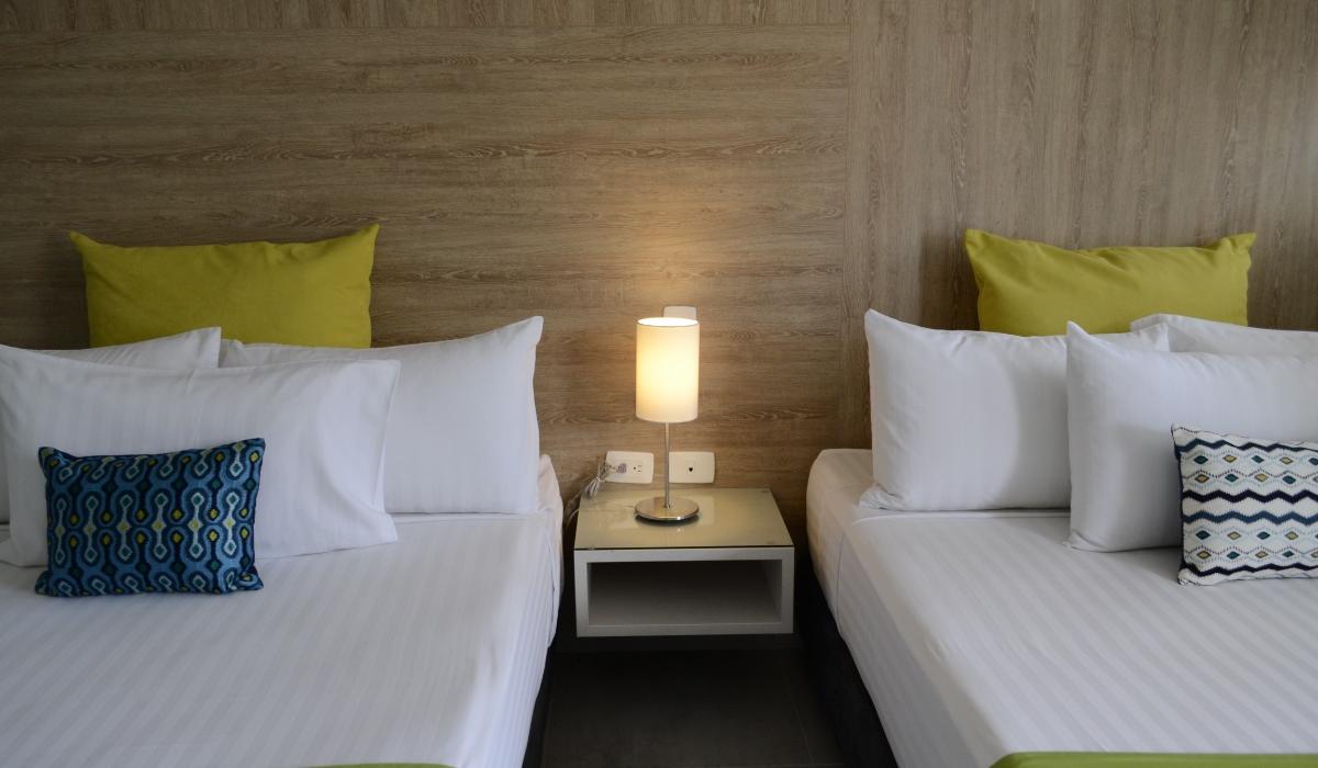 Habitación doble con decoración colorida en Hotel Casablanca Cúcuta. Habitación con dos camas dobles, almohadas verdes y cojines estampados en Hotel Casablanca Cúcuta.