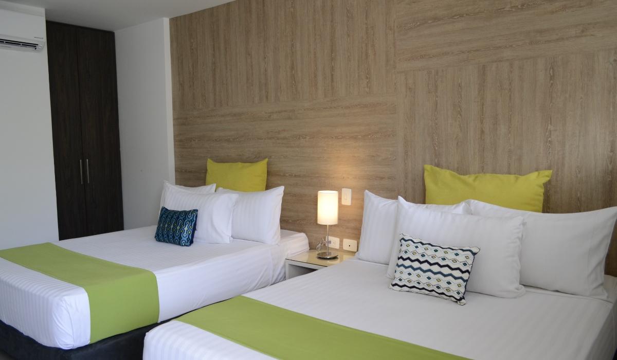 Habitación doble con decoración moderna y camas confortables en Hotel Casablanca Cúcuta. Habitación doble con camas amplias, almohadas verdes y lámpara central en Hotel Casablanca Cúcuta.